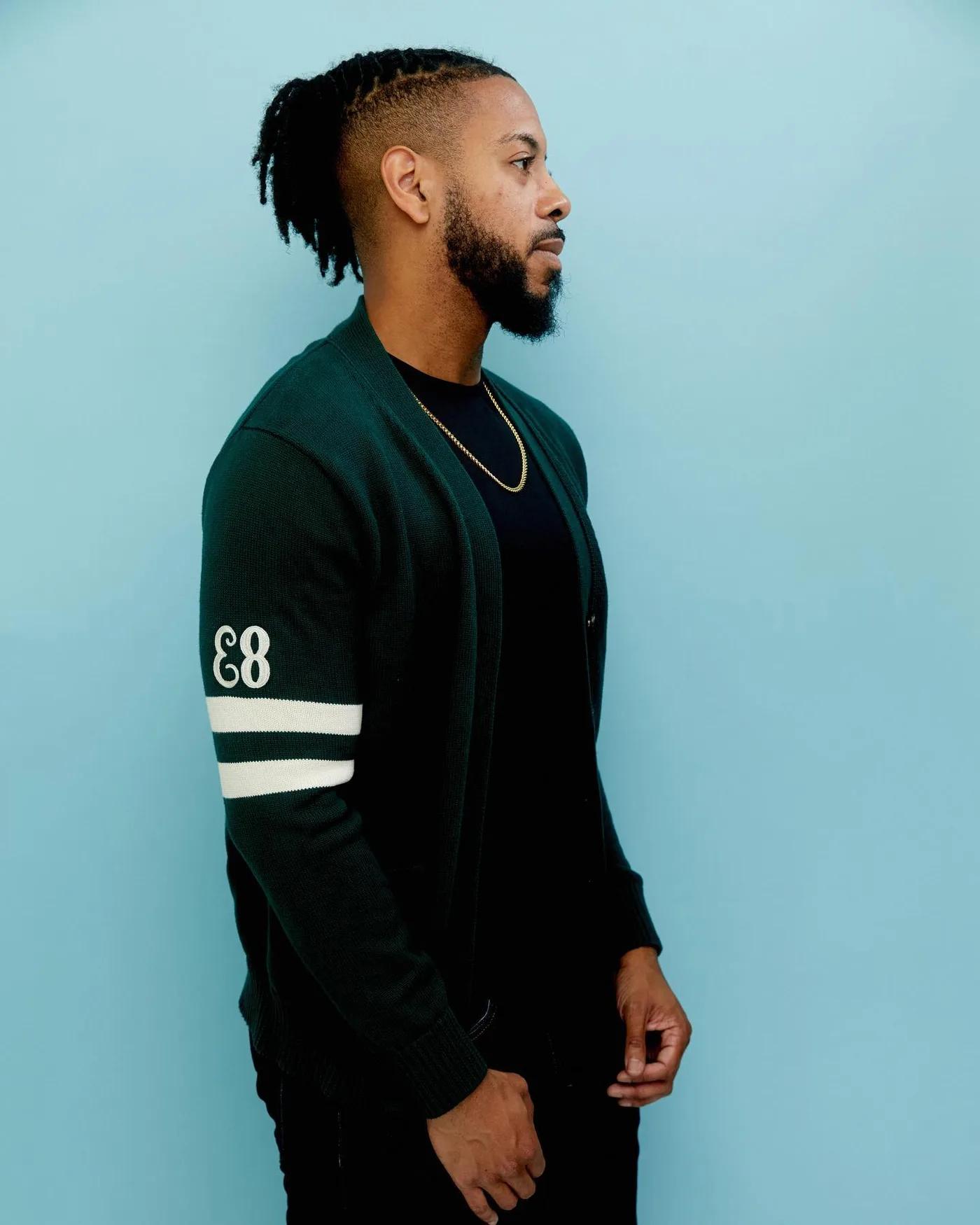William in profile wearing a green sweater with his locs tied back